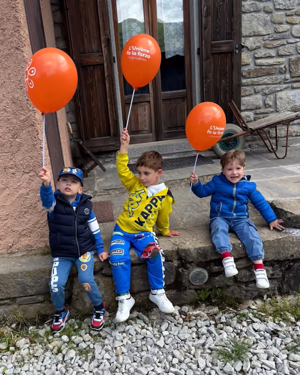 Tre bambini con palloncini arancioni durante la giornata di Mielerie Aperte