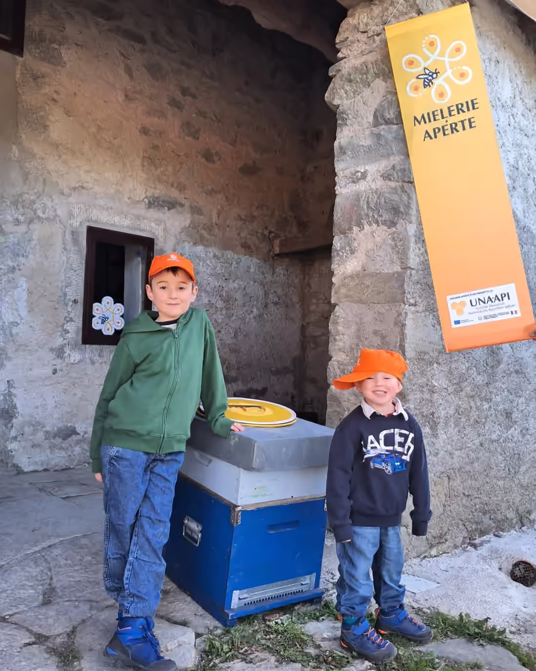 Due bambini con il cappello davanti a un’arnia, durante la giornata di Mielerie Aperte