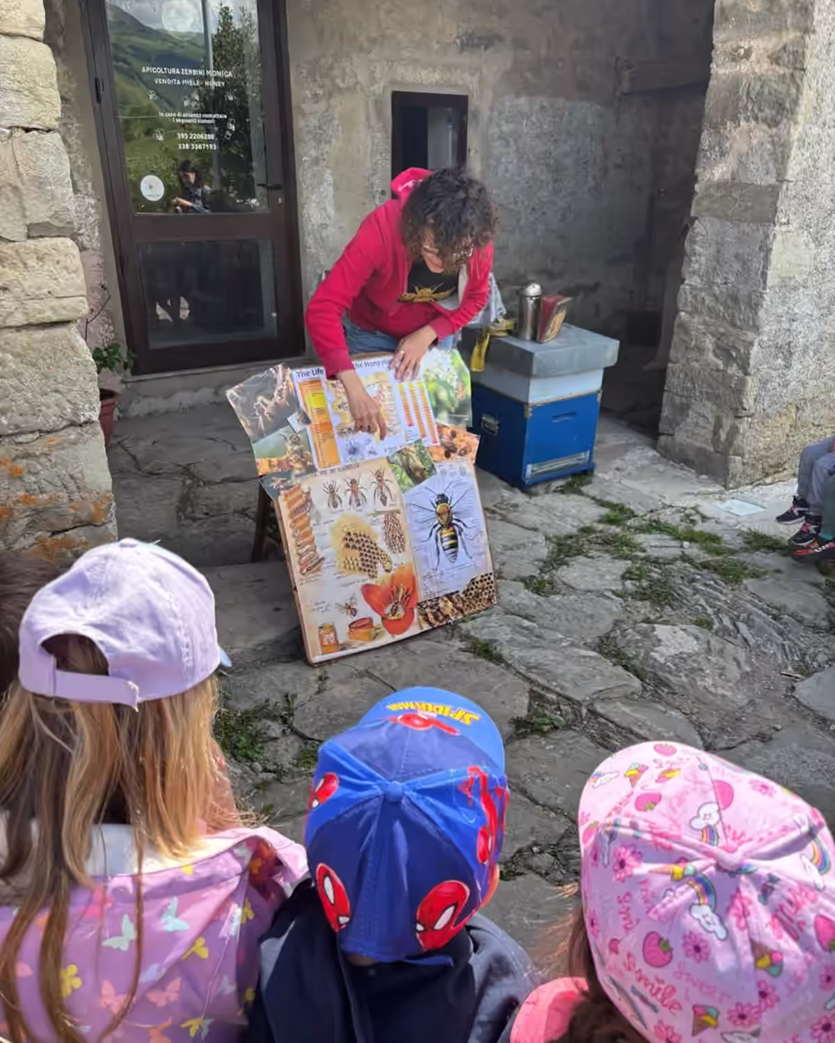 Un cartellone con immagini di api e miele mostrato a tre bambini