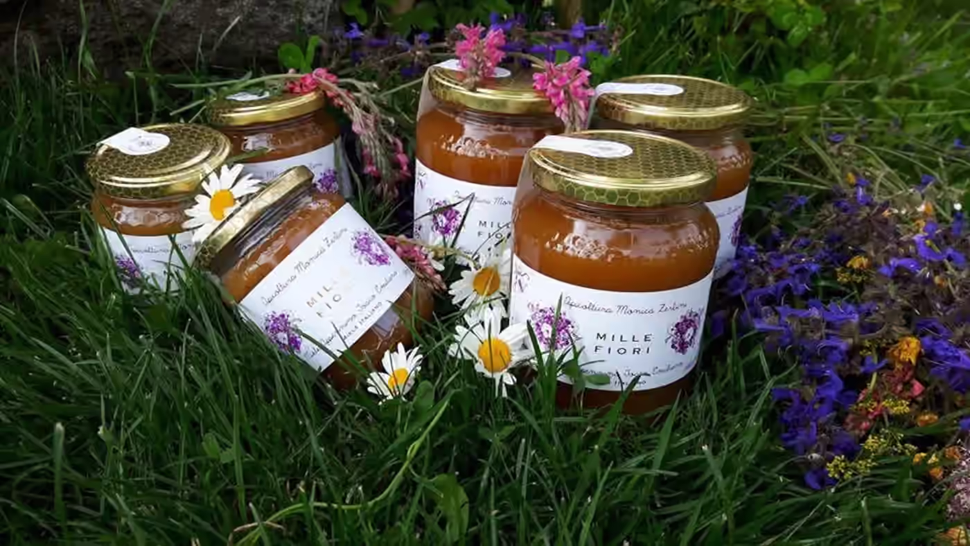 Vasetti di miele millefiori con etichetta tra fiori di campo ed erba